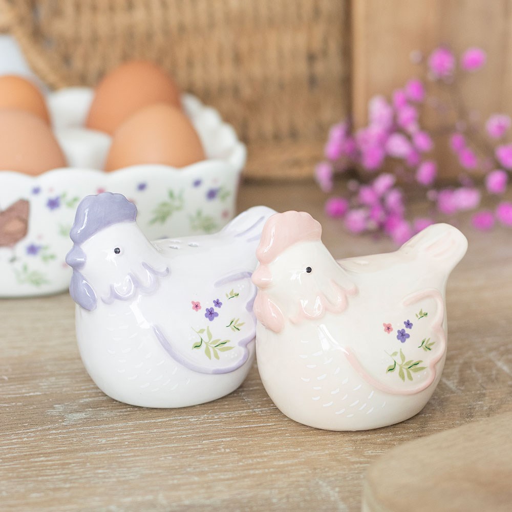 Two ceramic chicken figurines with floral designs on a wooden surface with eggs in the background.