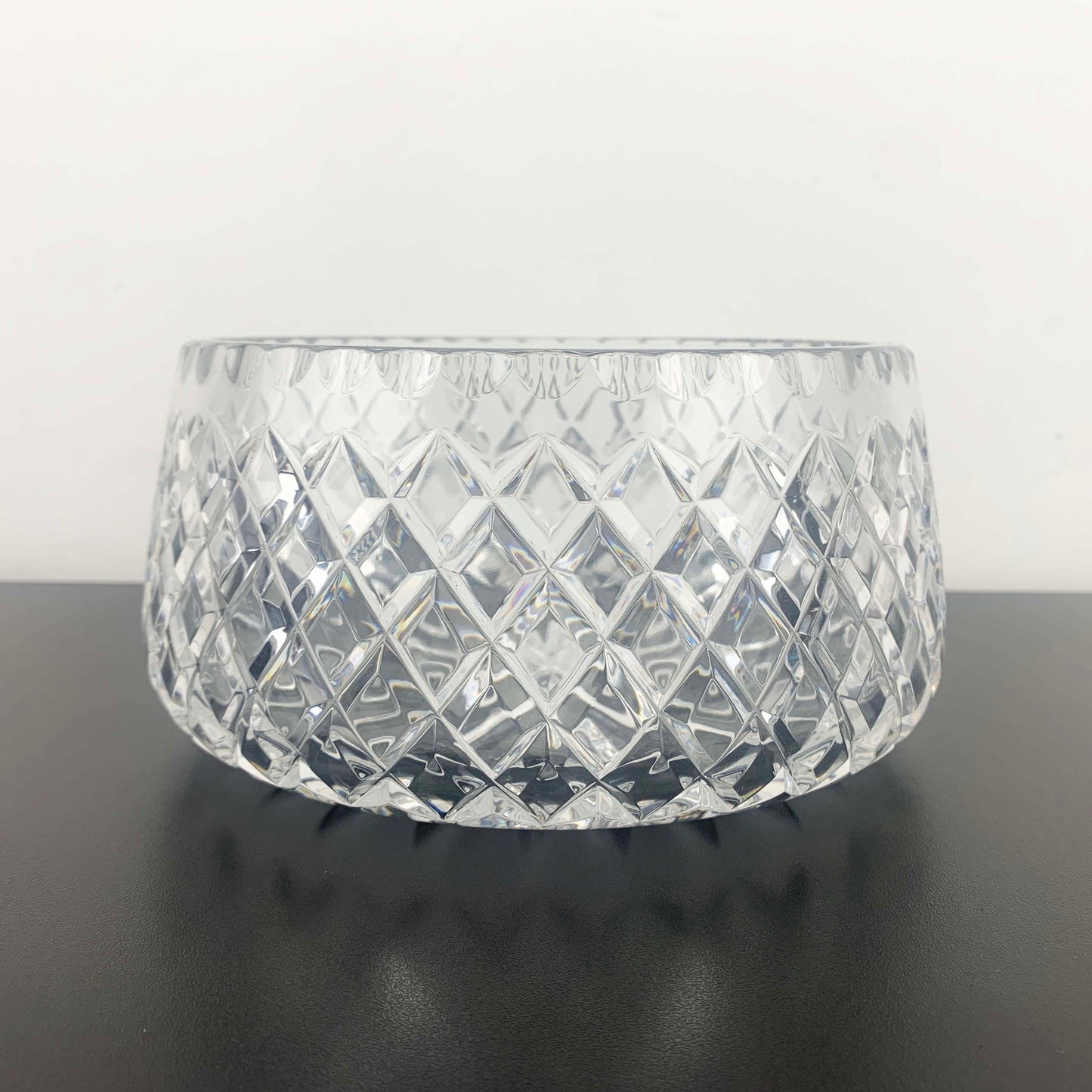 Clear glass bowl with diamond pattern on a black surface and white background