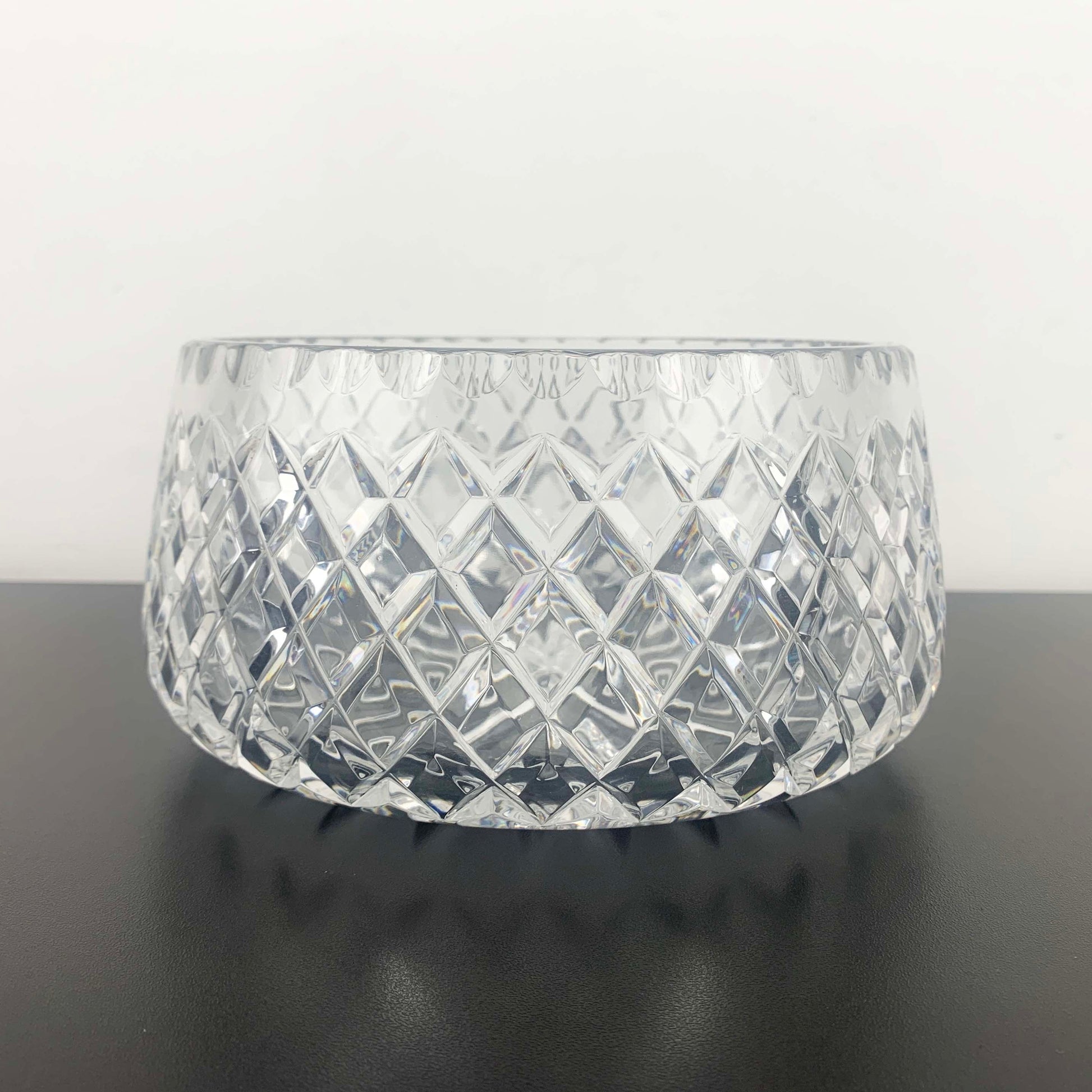 Clear glass bowl with diamond pattern on a black surface and white background