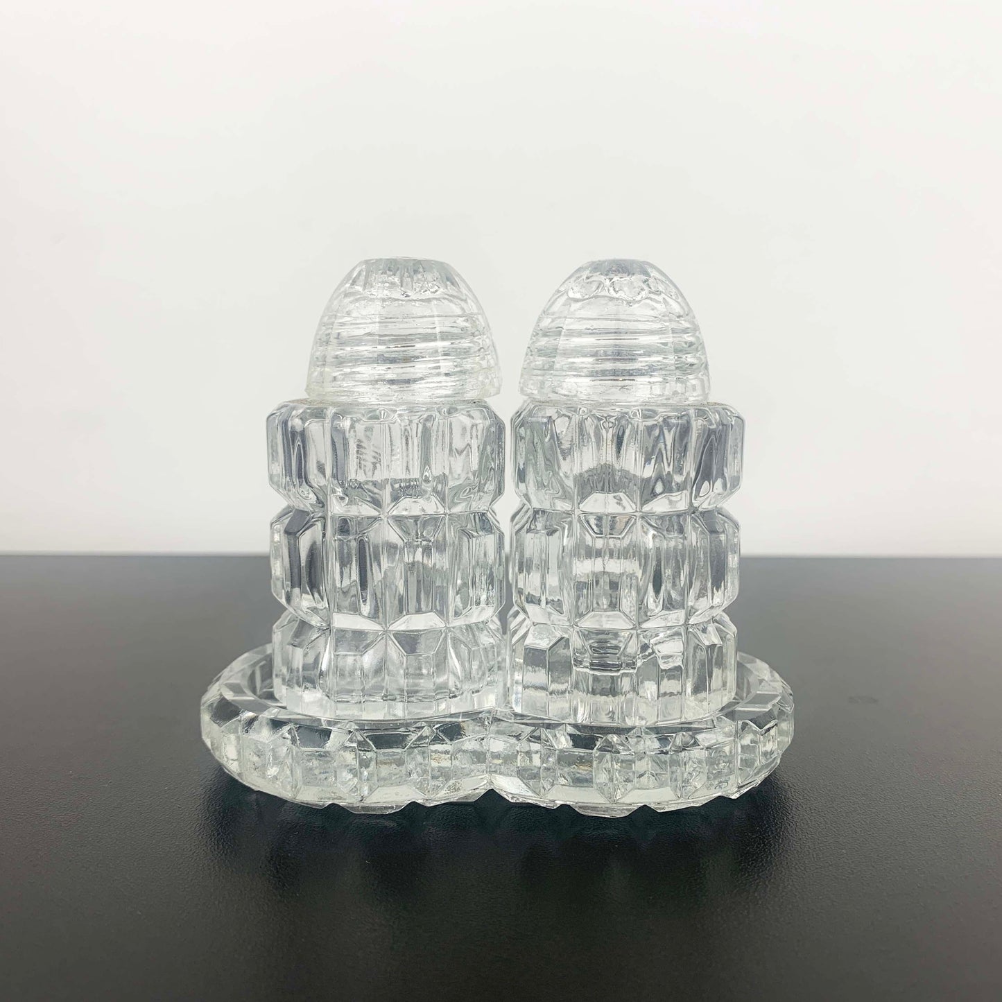 Clear glass salt and pepper shakers on a matching tray against a white background