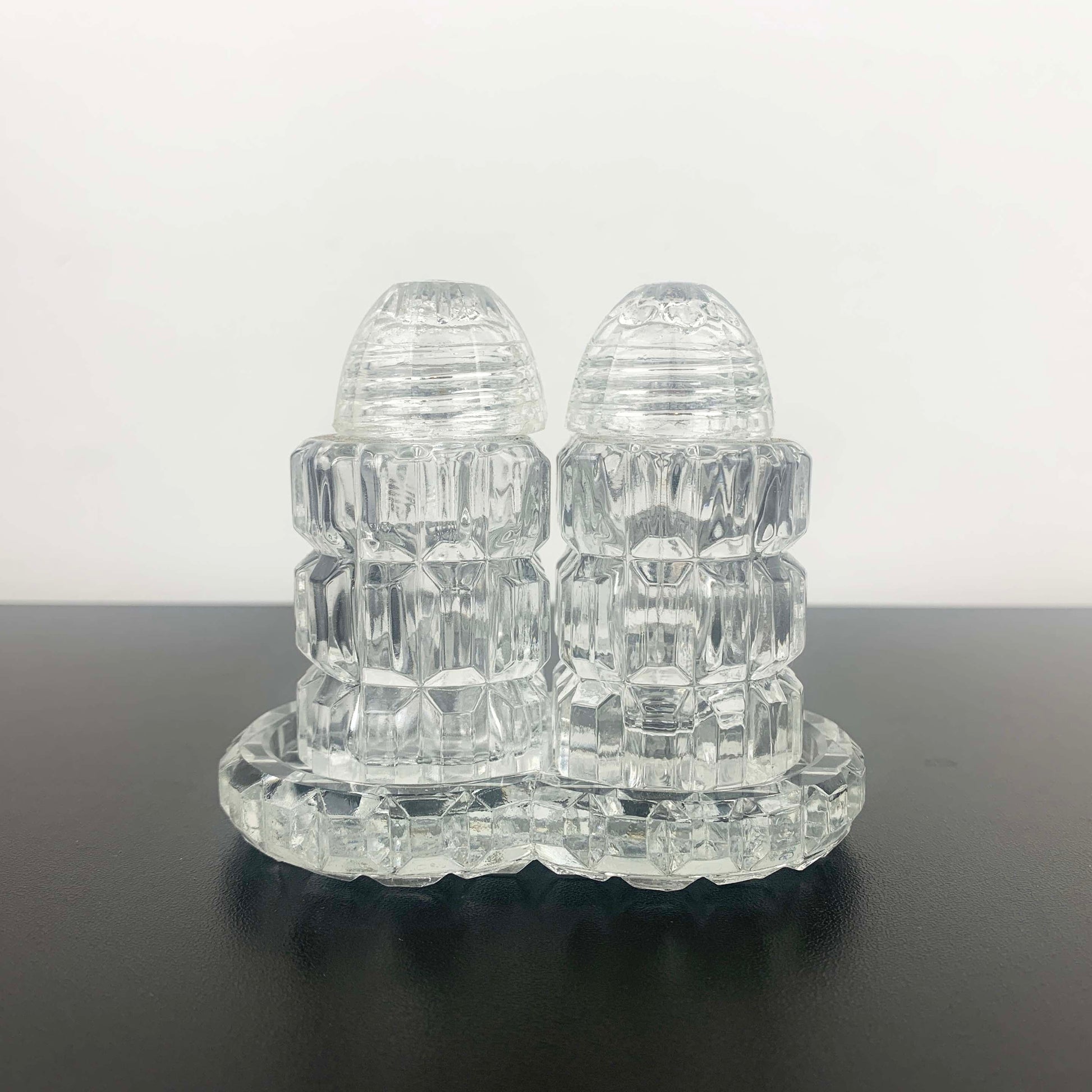 Clear glass salt and pepper shakers on a matching tray against a white background