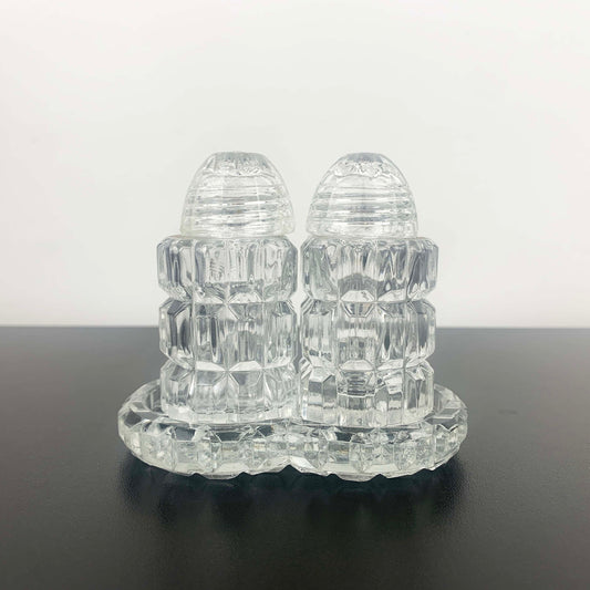 Clear glass salt and pepper shakers on a matching tray against a white background