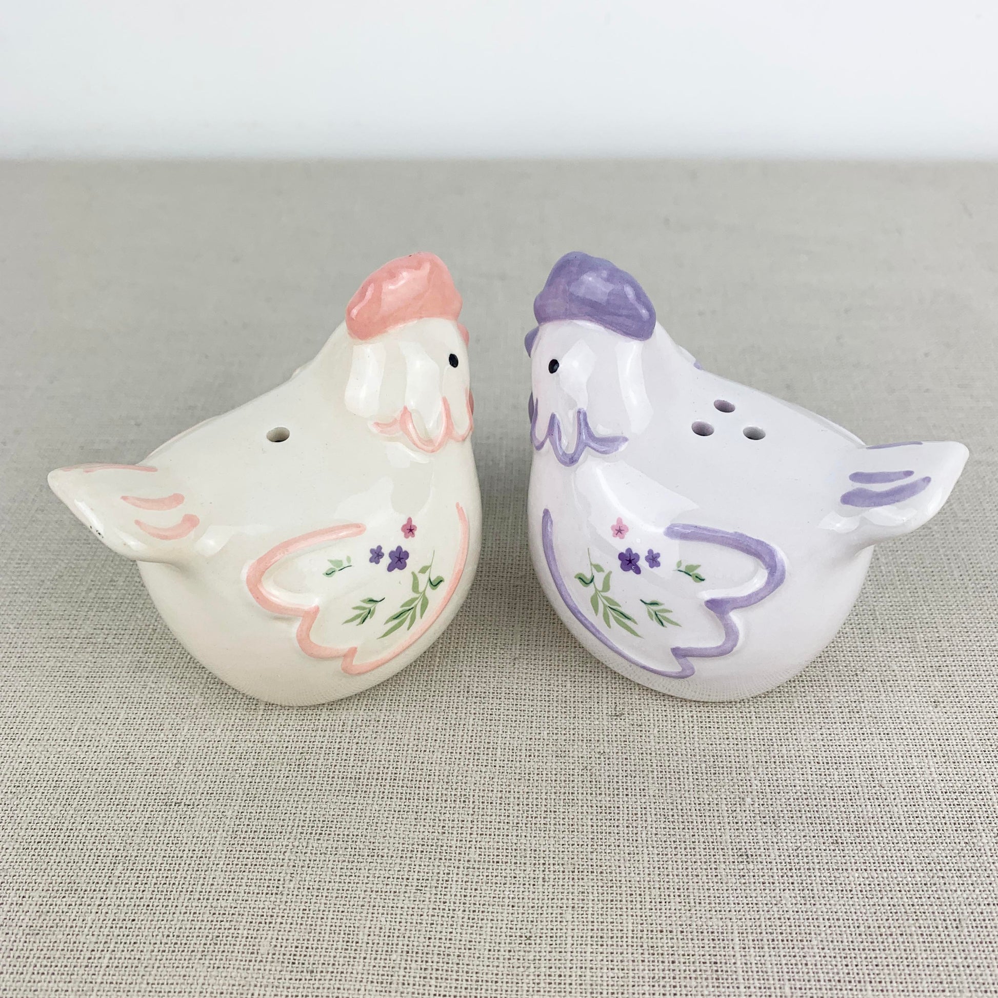 Two ceramic chicken-shaped salt and pepper shakers on a textured surface.