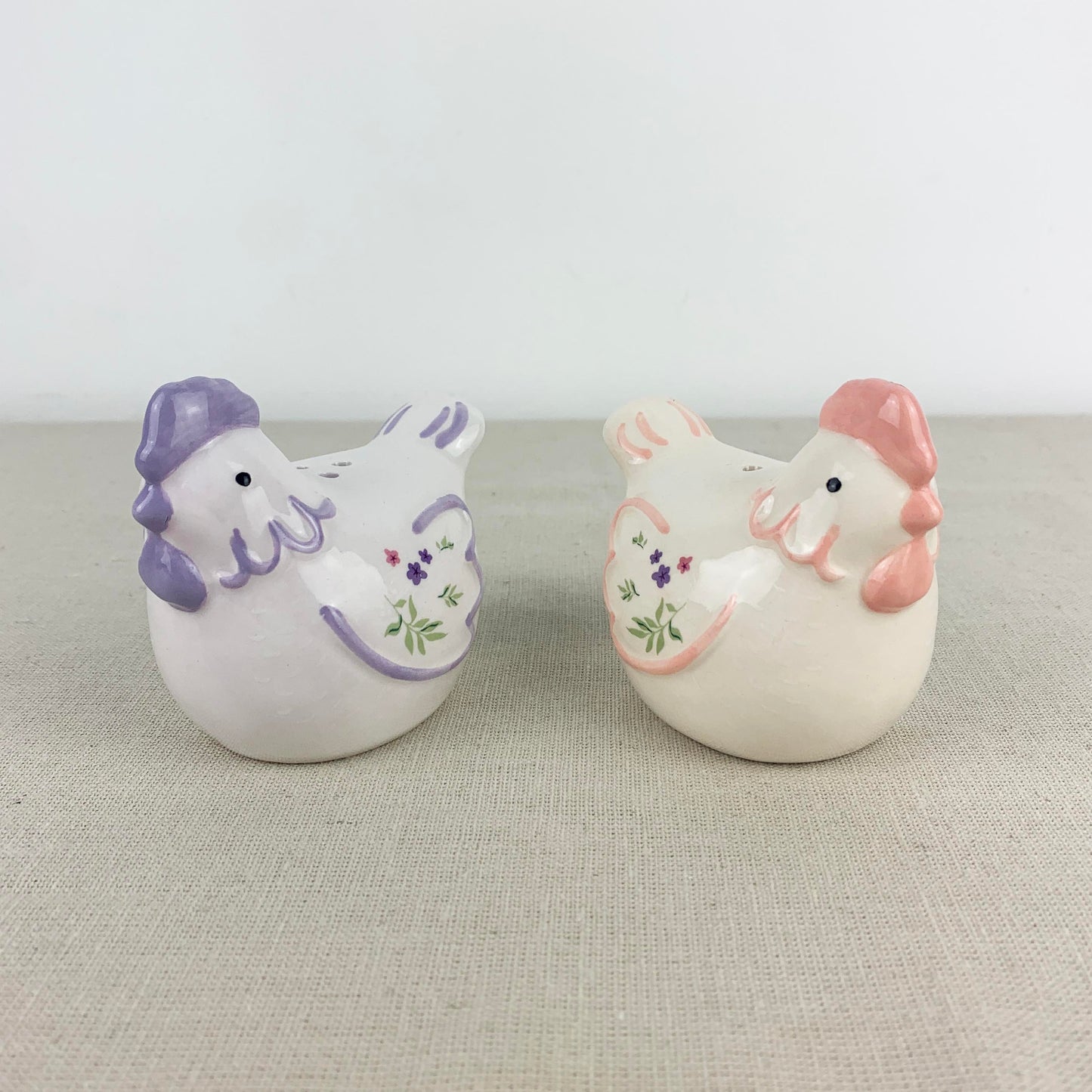 Two ceramic chicken figurines with decorative elements on a neutral background