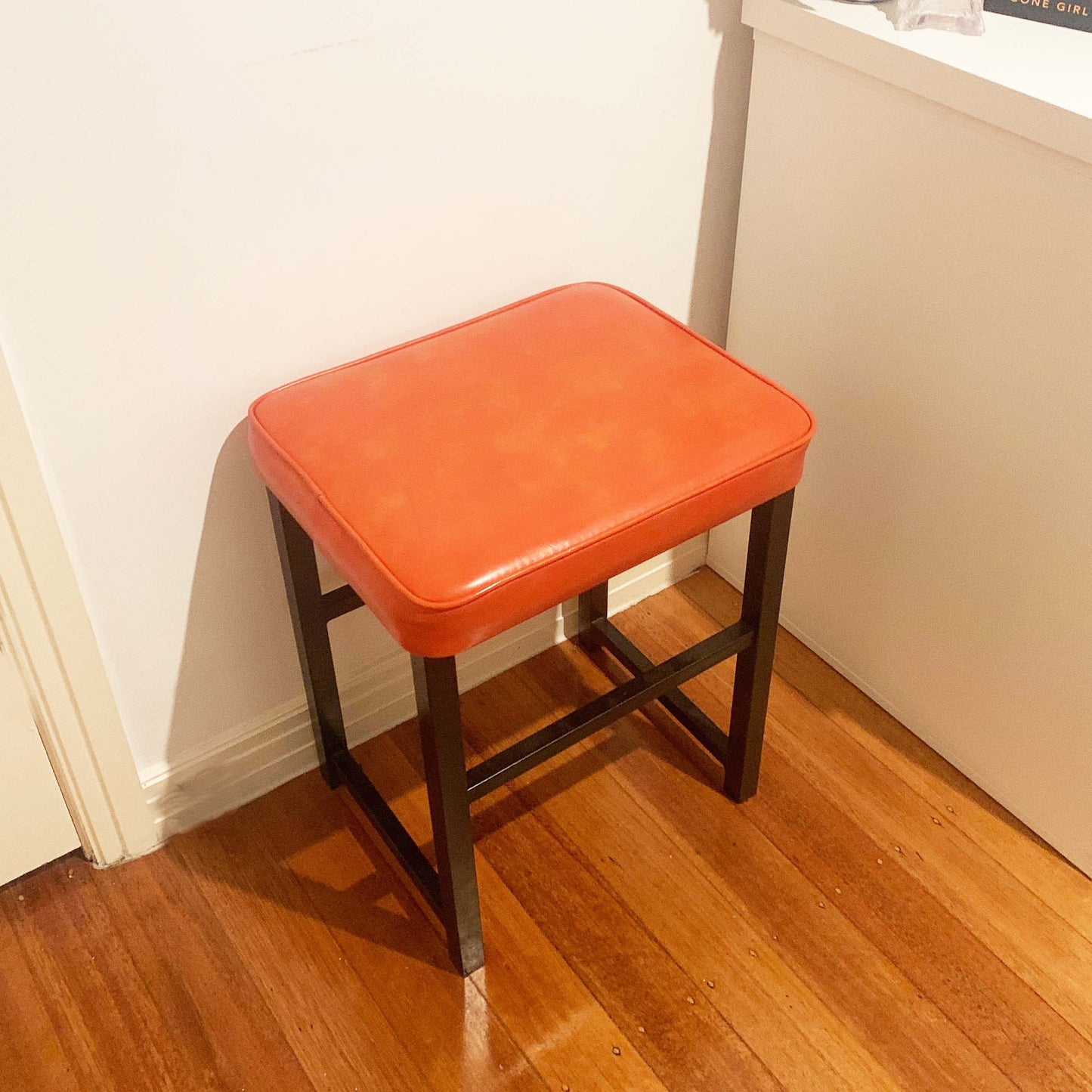 Upholstered mid century orange vinyl stool with black metal legs