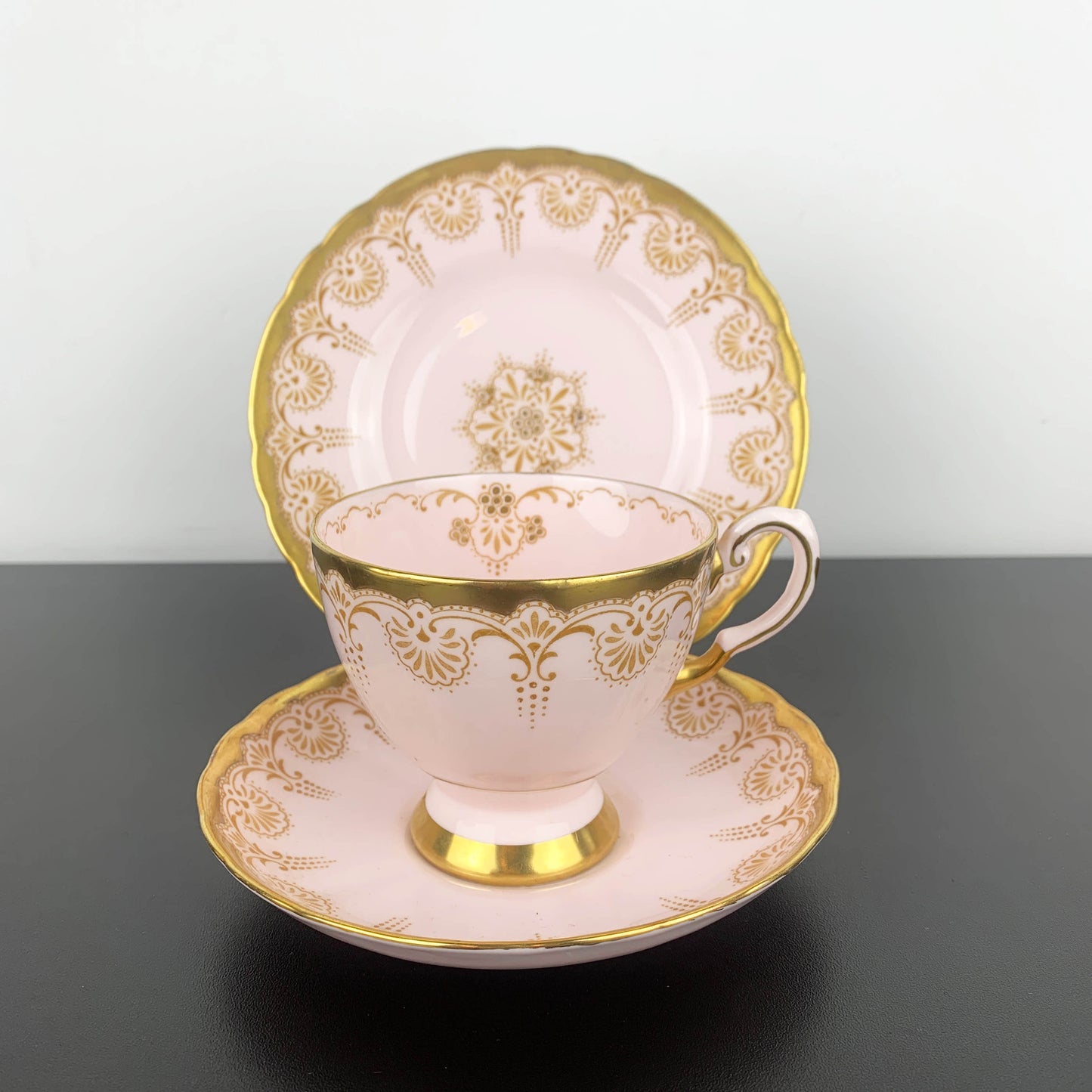 Teacup and saucer set with gold intricate patterns on a dark surface.