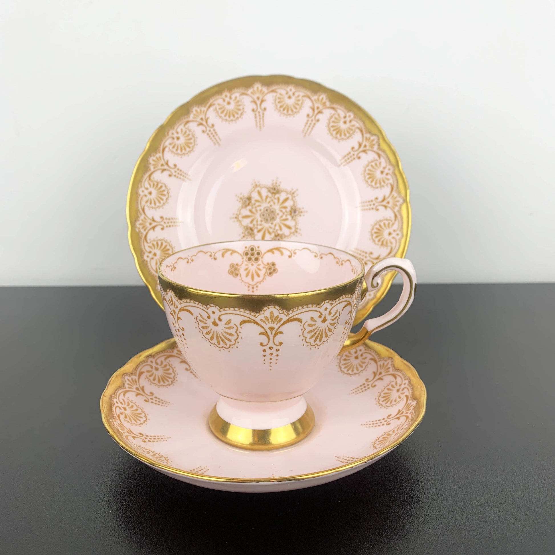 Teacup and saucer set with gold intricate patterns on a dark surface.