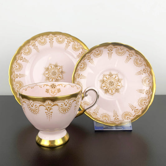 Ceramic cup and saucers with gold floral patterns on a gray surface.