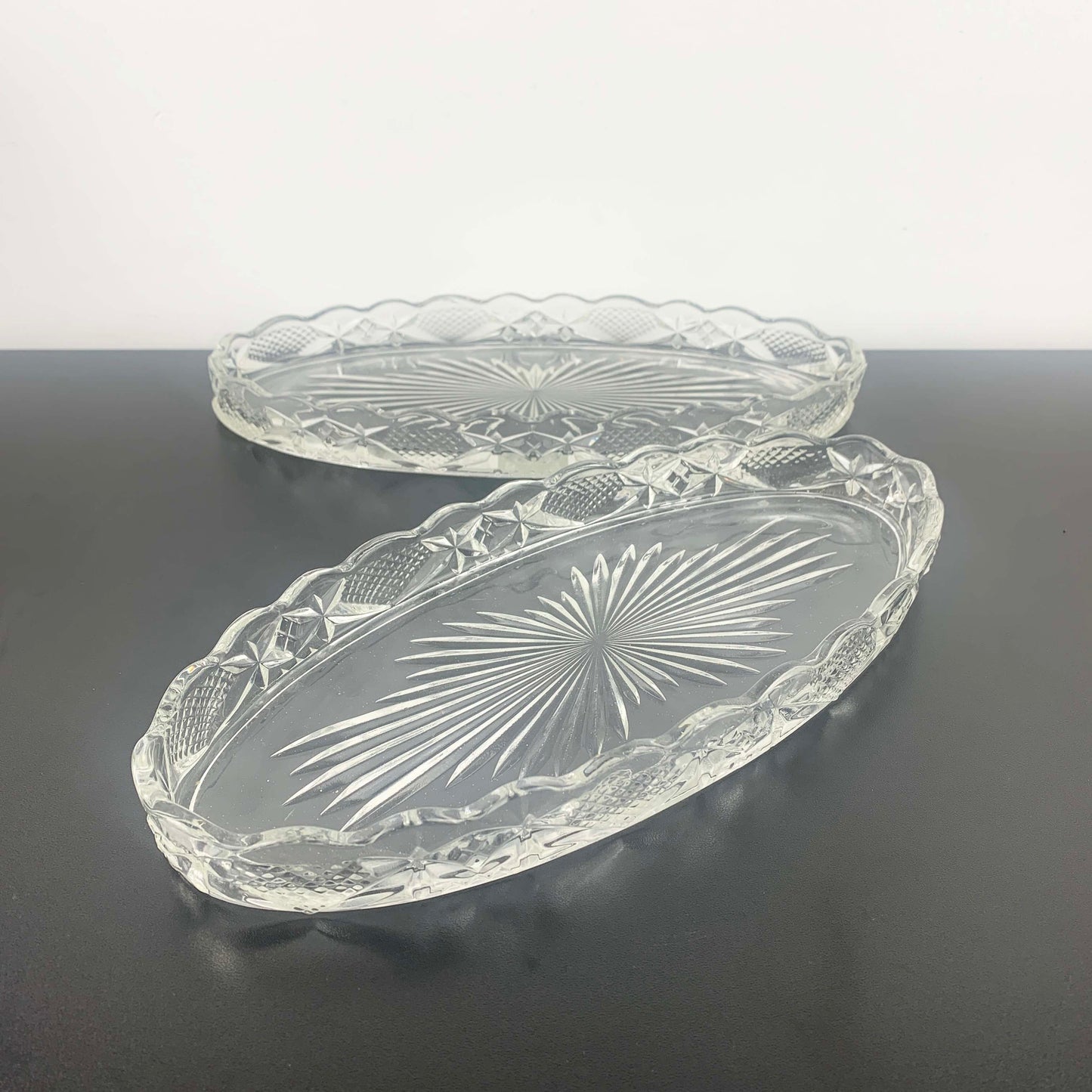 Two clear glass trays with embossed designs on a dark surface.