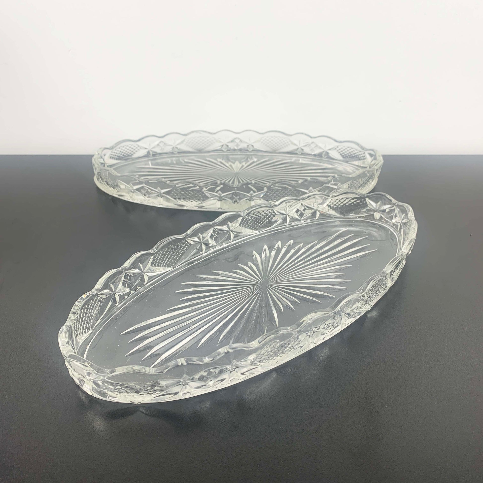 Two clear glass trays with embossed designs on a dark surface.