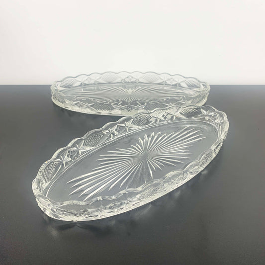 Two clear glass trays with embossed designs on a dark surface.