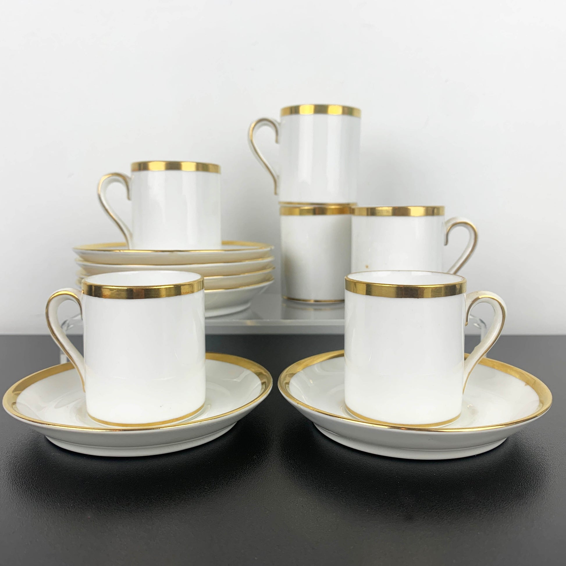 Set of white ceramic cups and saucers with gold rims on a dark surface.