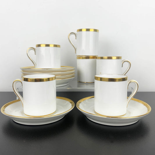 Set of white ceramic cups and saucers with gold rims on a dark surface.