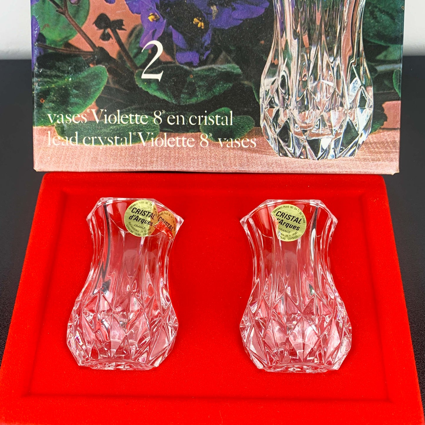 Two crystal vases on a red cushion with packaging in the background