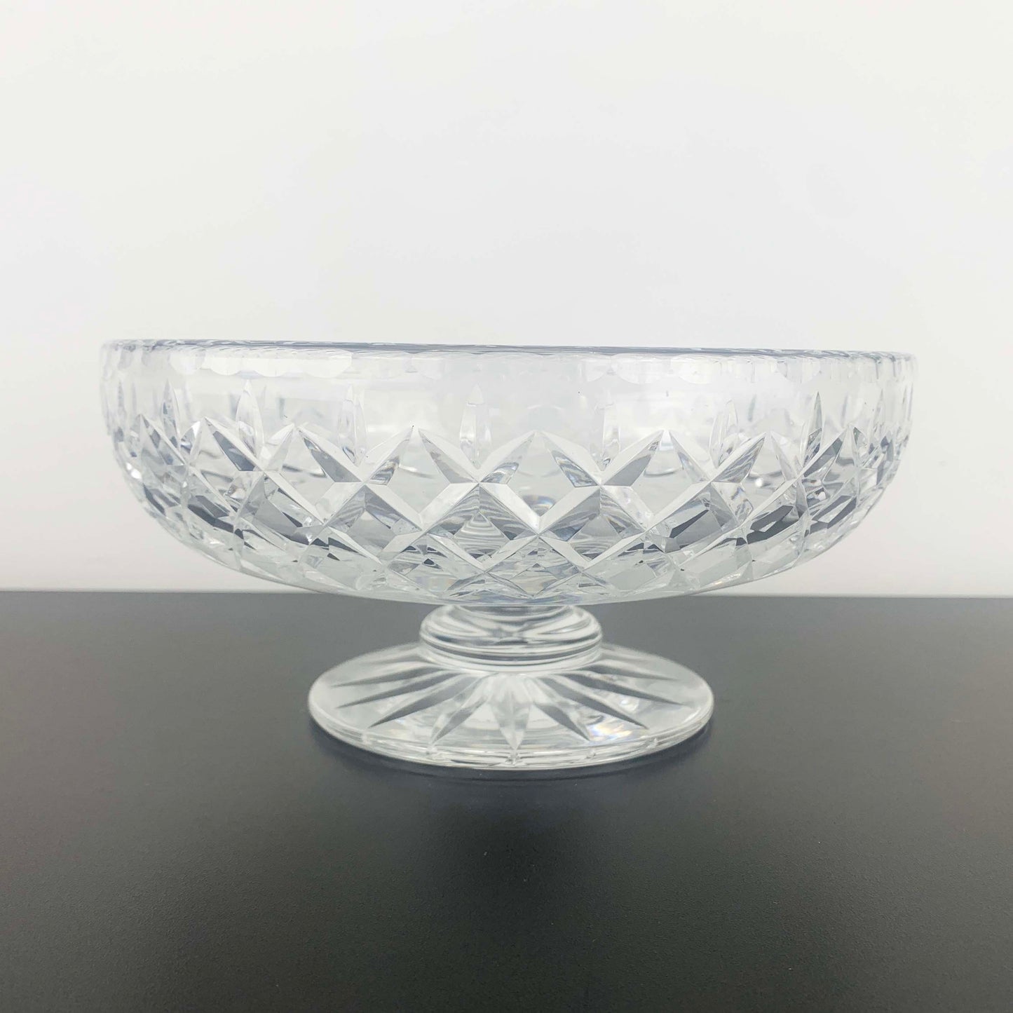 Clear glass bowl with diamond pattern on a dark surface and light gray background