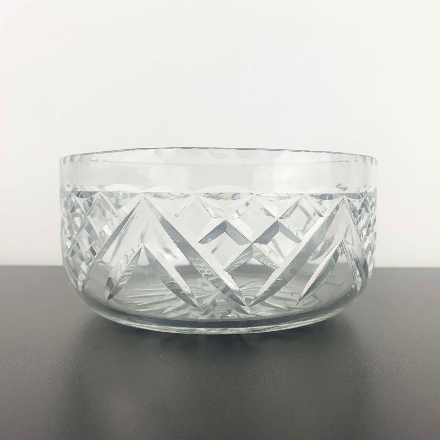 Clear glass bowl with geometric patterns on a dark surface and light gray background