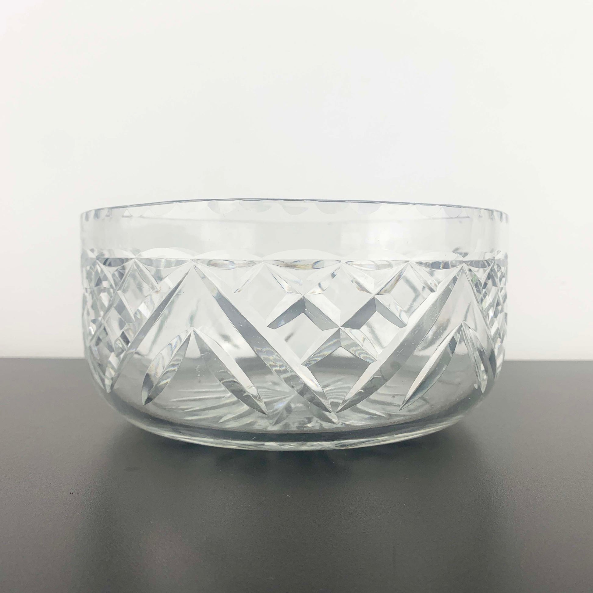 Clear glass bowl with geometric patterns on a dark surface and light gray background